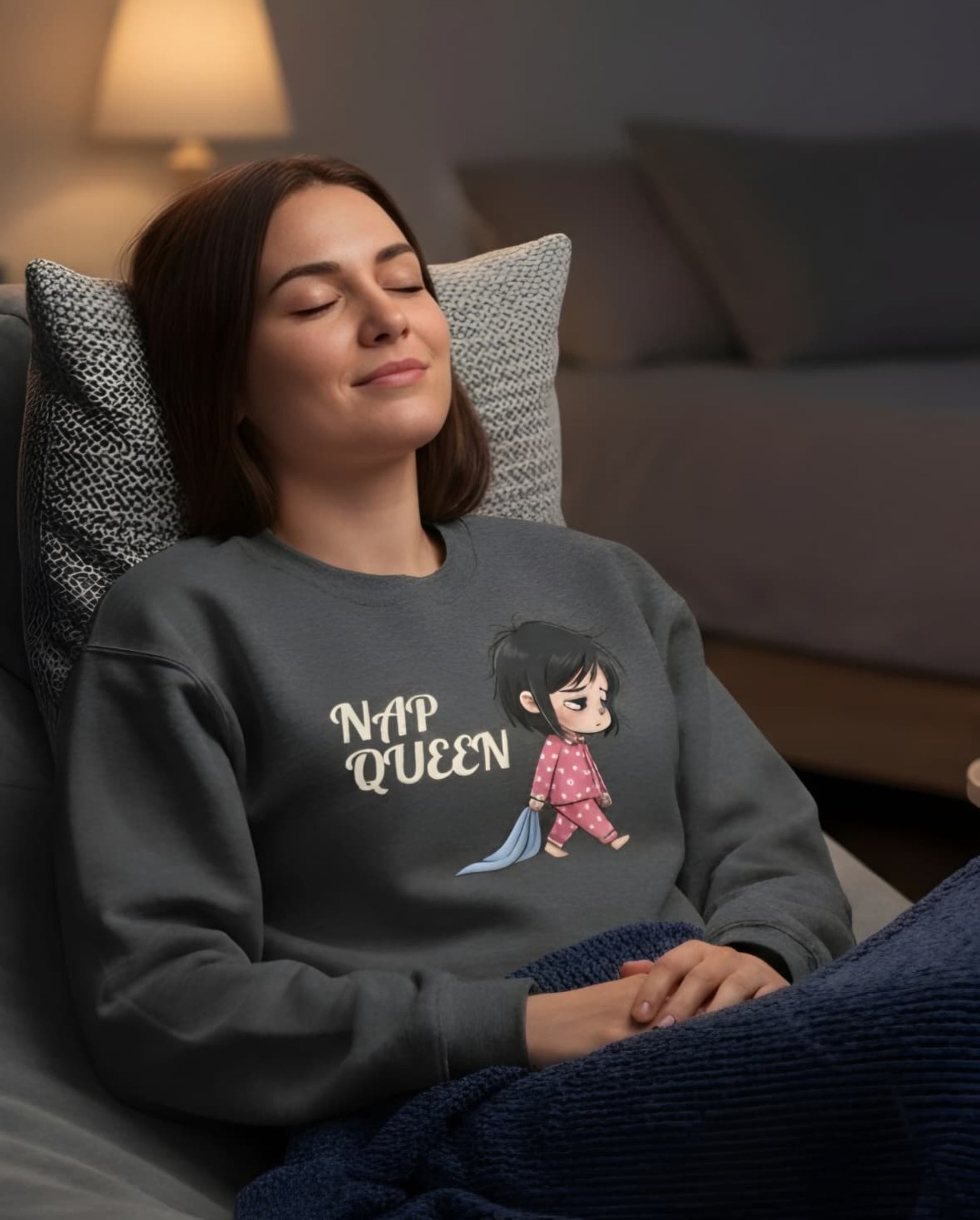 Woman wearing a sweatshirt with 'Nap Queen' and a cartoon character, sitting on a couch.